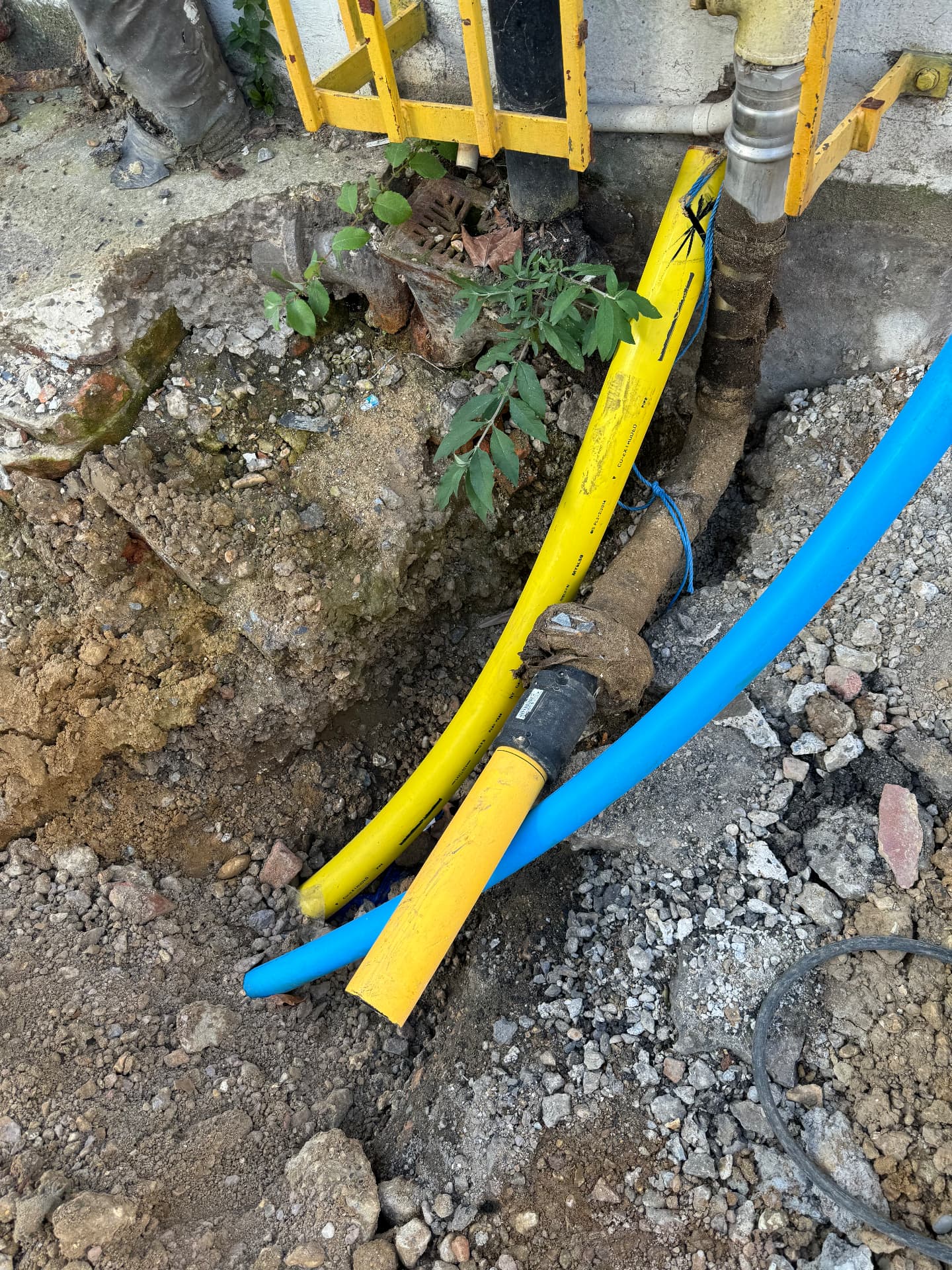 Excavated yellow PE gas pipe with electrofusion joint rising to a steel above-ground termination