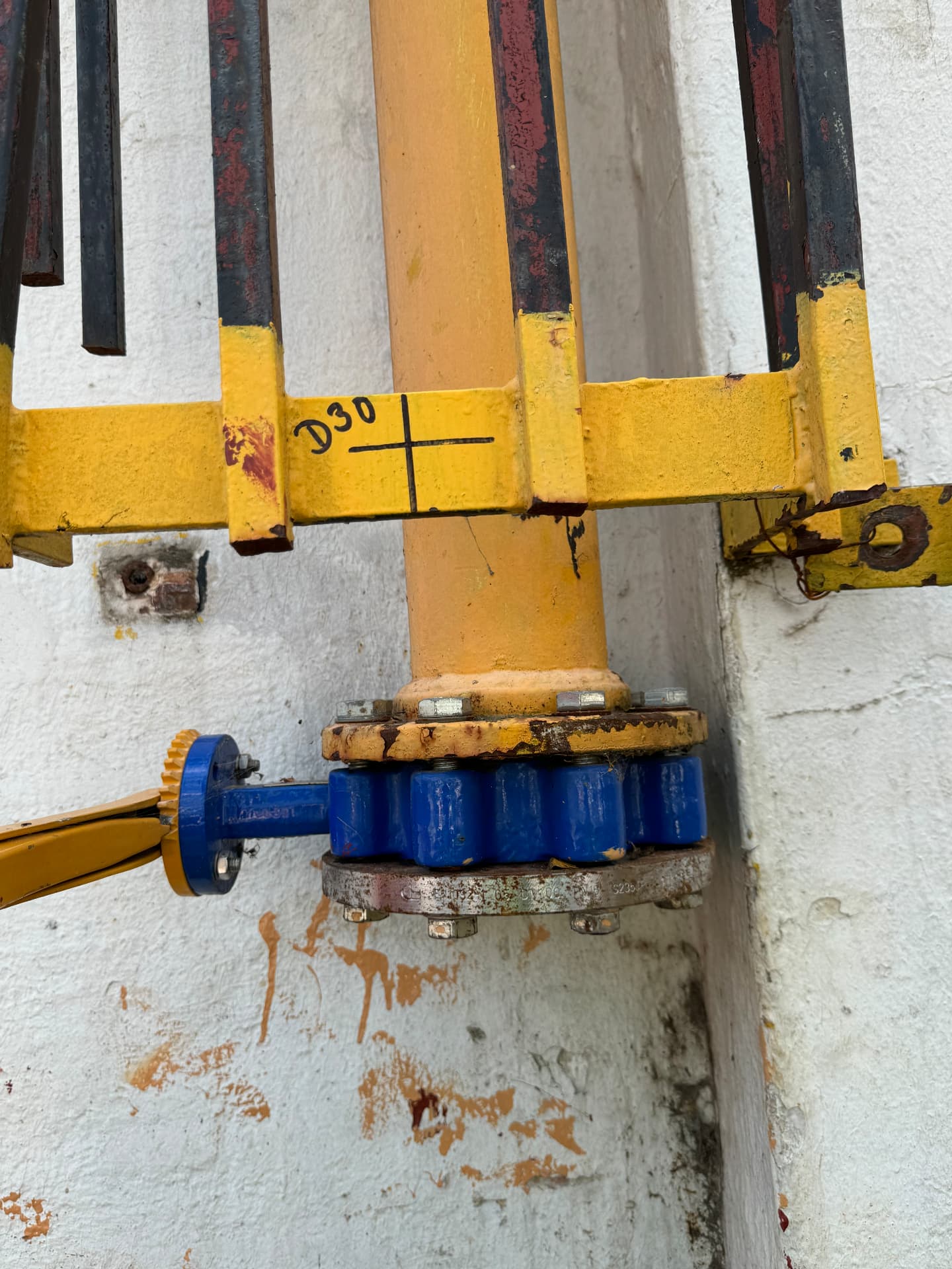 Blue flanged butterfly valve on yellow gas pipework behind a protective steel guard
