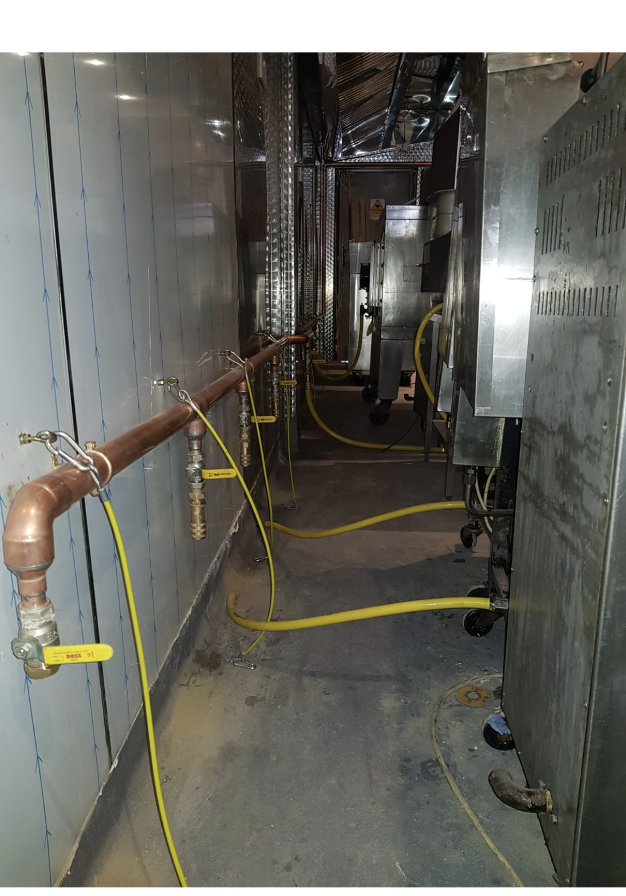 Copper gas distribution pipe with chained isolation valves and yellow hoses behind a commercial cookline