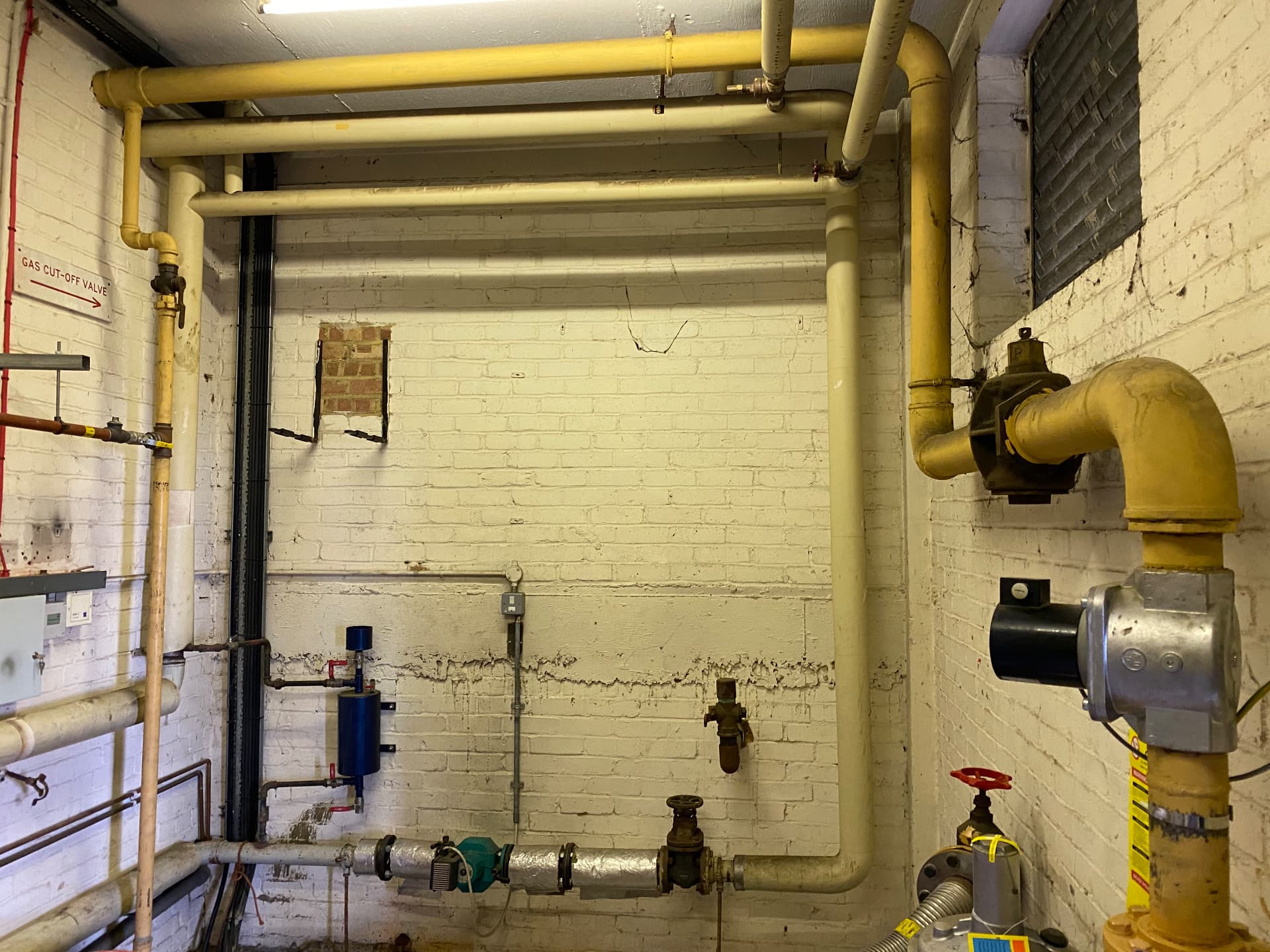 Commercial gas booster on yellow pipework in a basement plant room